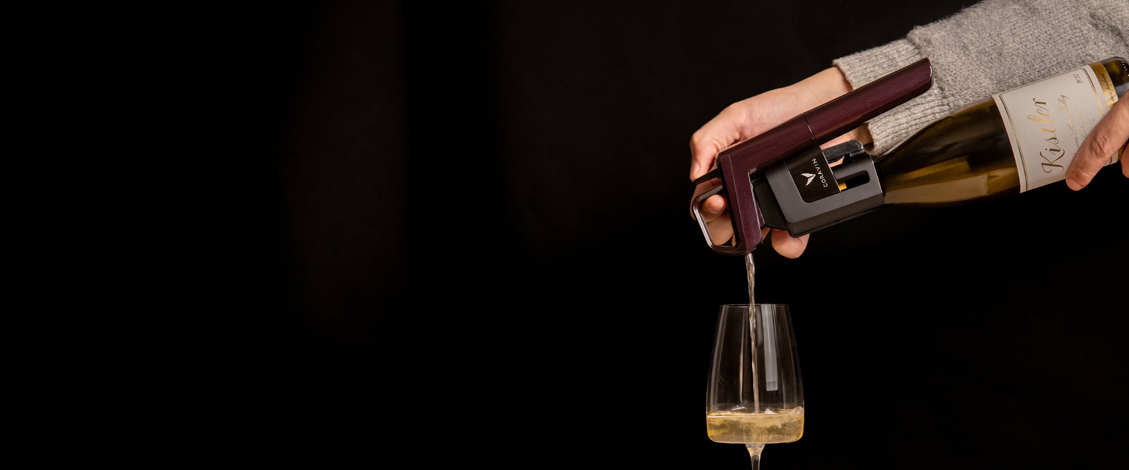 Person pouring wine from a bottle into a glass against a black background