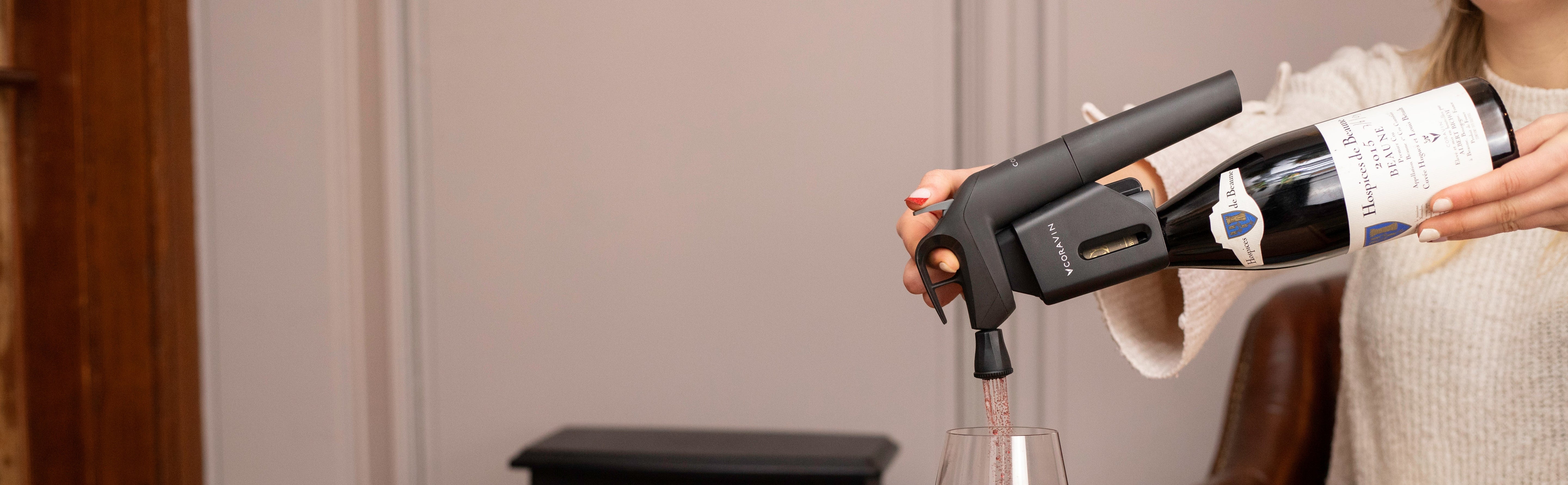 A person pours red wine into a glass using a sleek wine aerator, with a bottle labeled "Hospices de Beaune" visible.