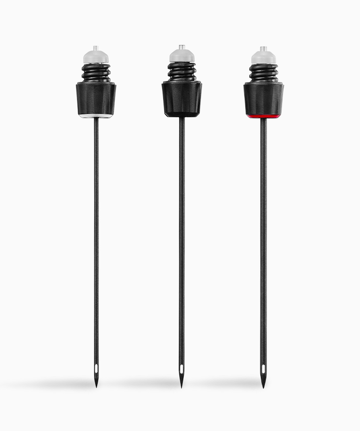 Three black food markers with clear tops, varying colors on the caps, resting on pointed black stakes.