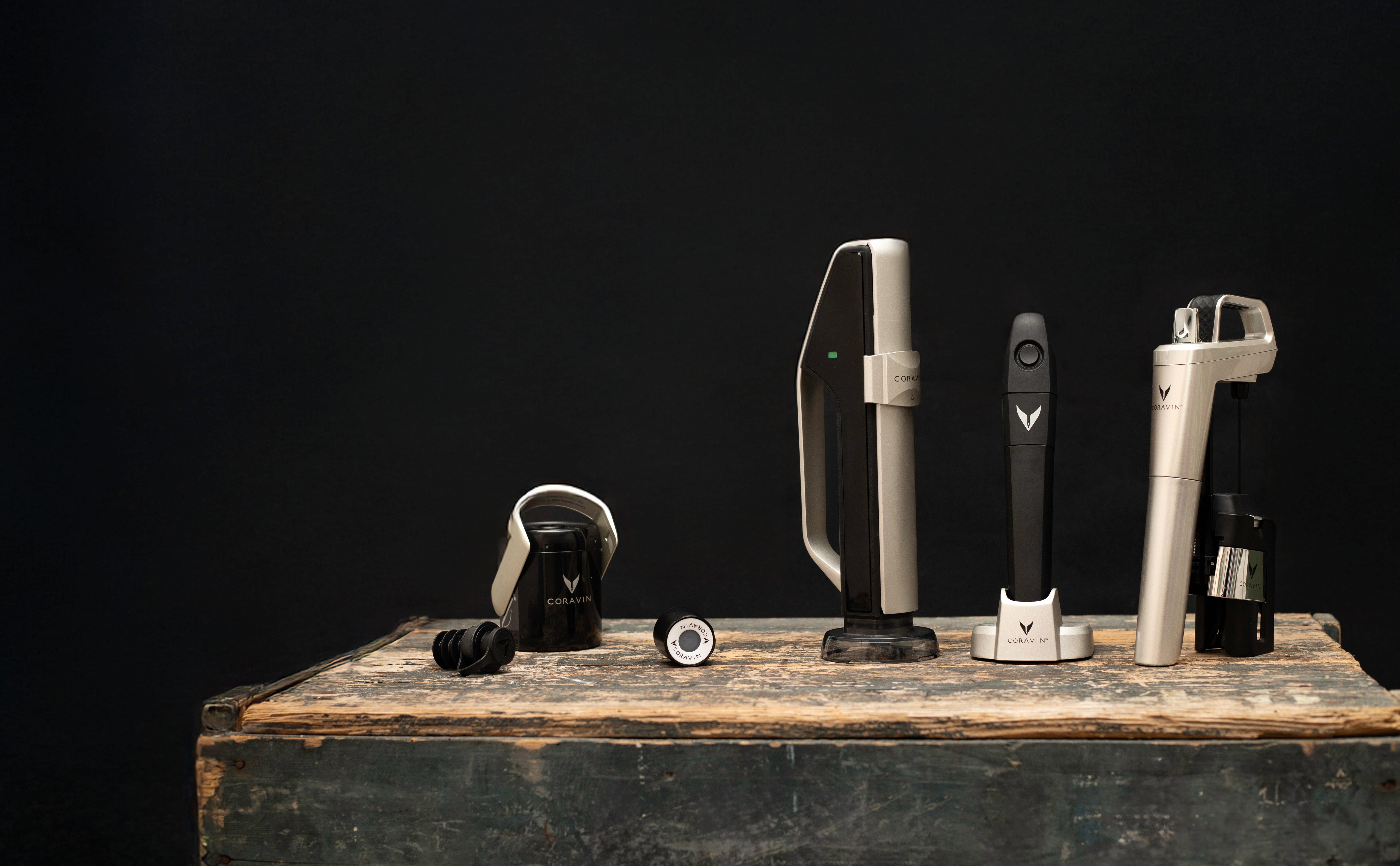 An arrangement of Coravin wine preservation tools on a rustic wooden surface, set against a dark background.