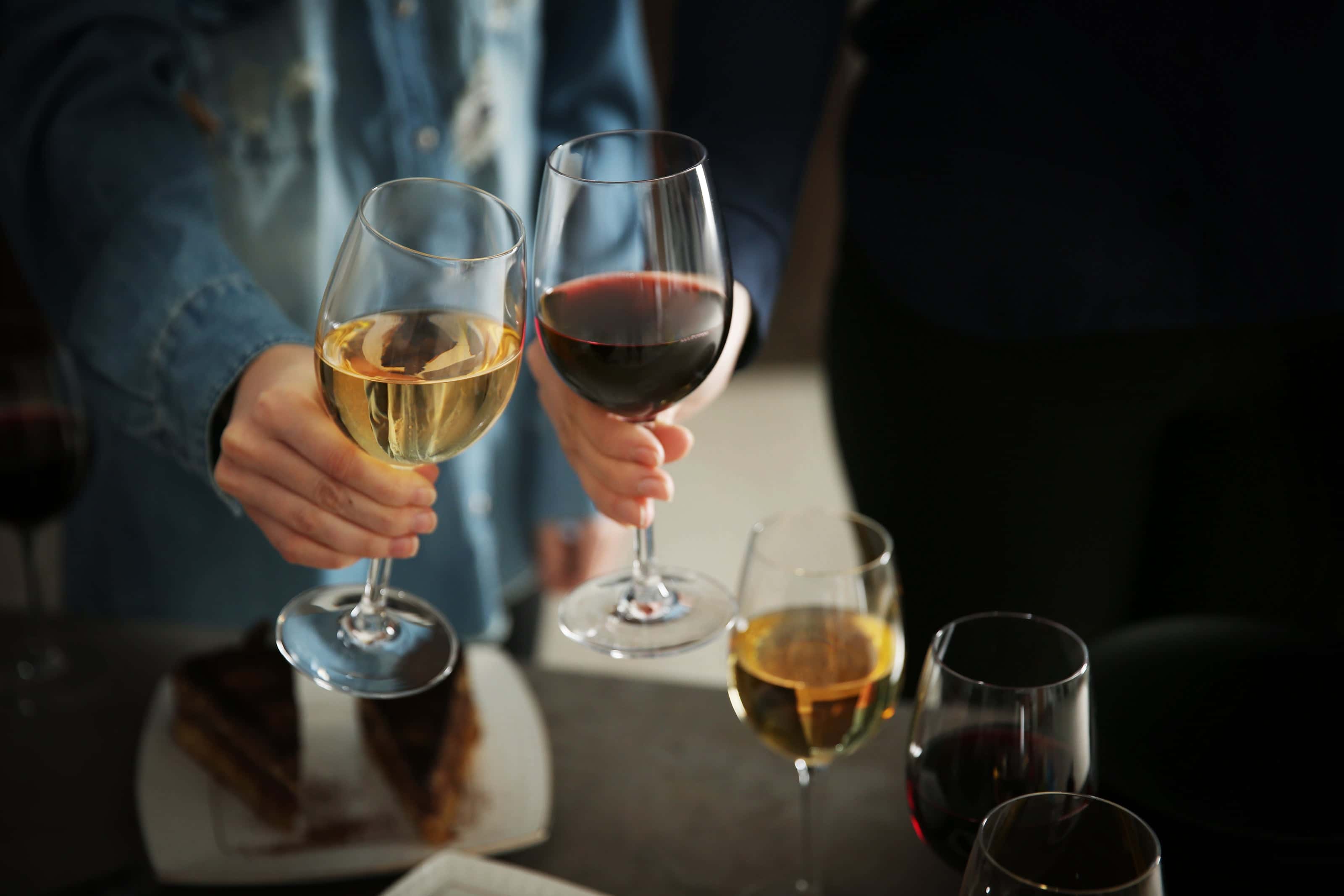 Two people clinking glasses of white and red wine at a casual wine and dessert gathering.