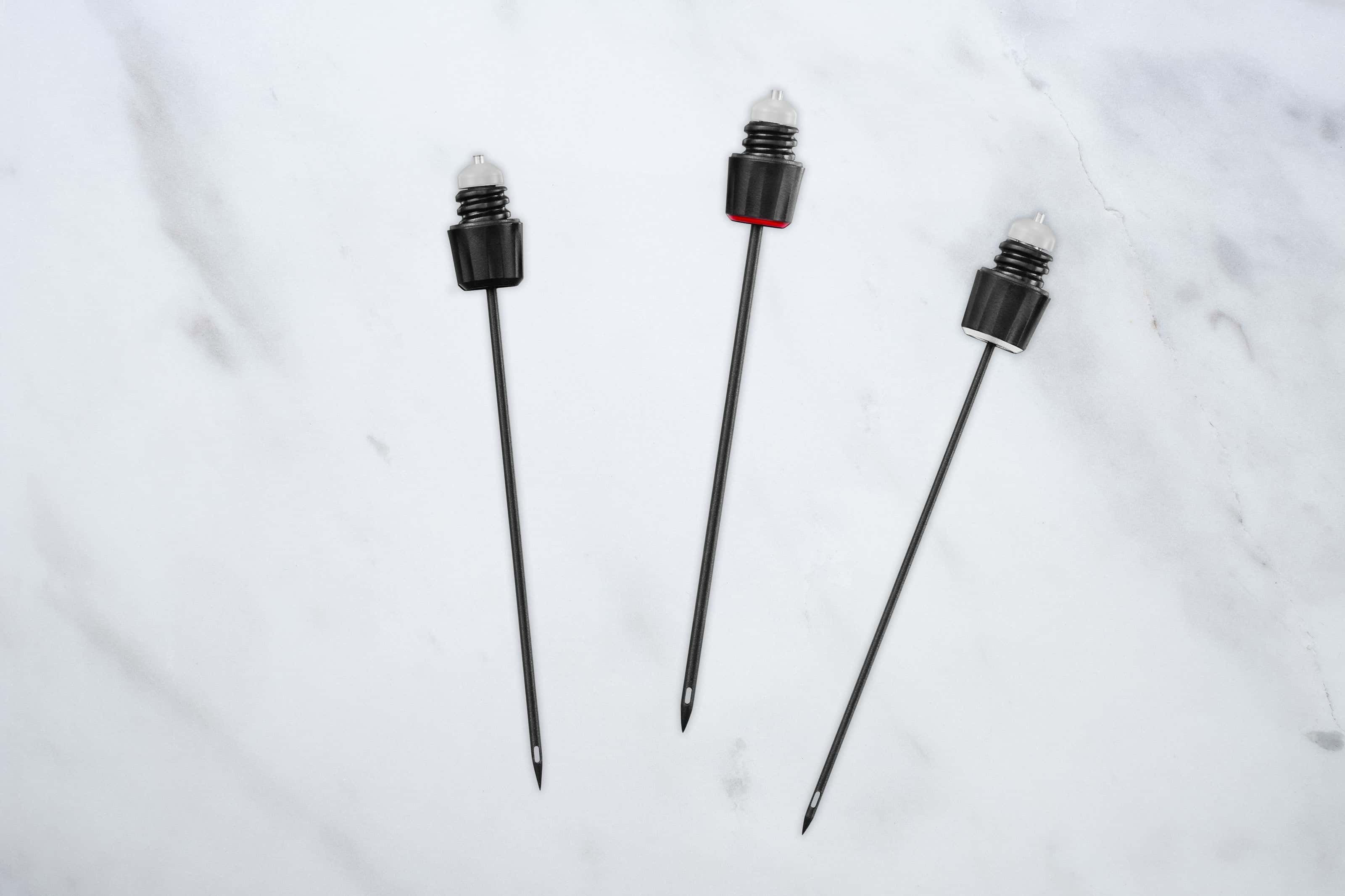 Three Coravin wine system needles with color-coded bands displayed on a white marble surface.