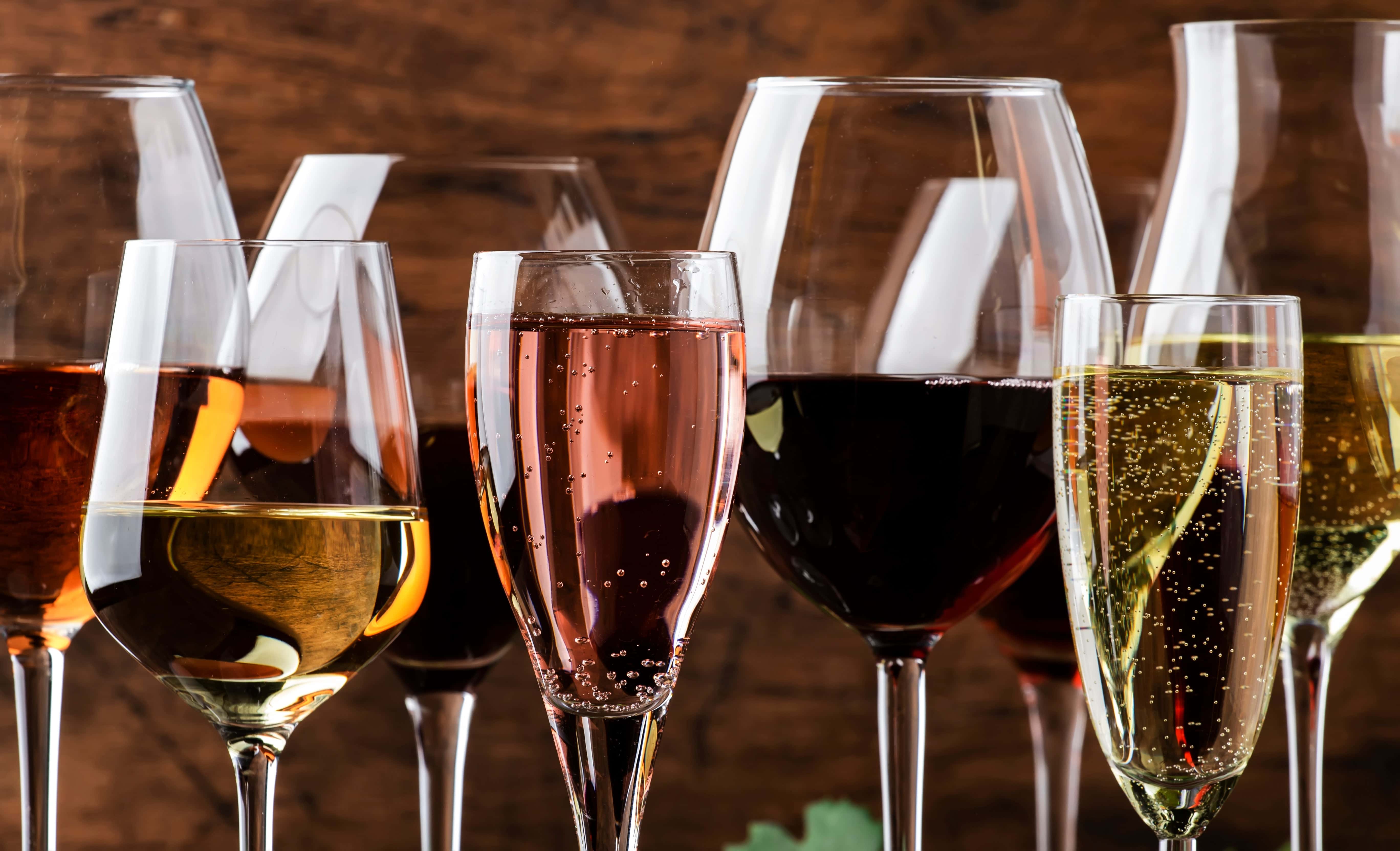 Assorted glasses of red, white, rosé, and sparkling wine against a rustic wooden background, showcasing wine variety and elegance.