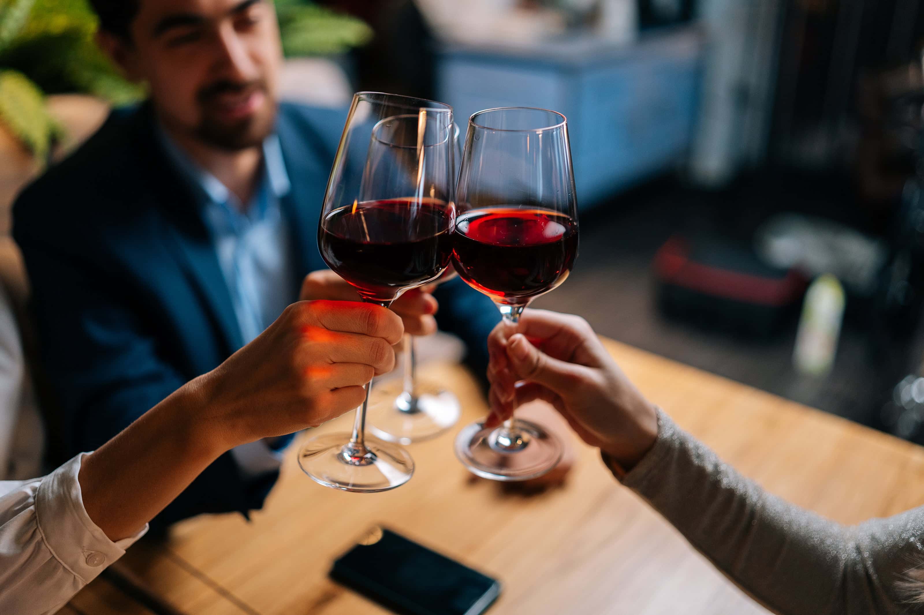 Group of friends clinking glasses of red wine at a wooden table in a cozy, upscale bar or restaurant.