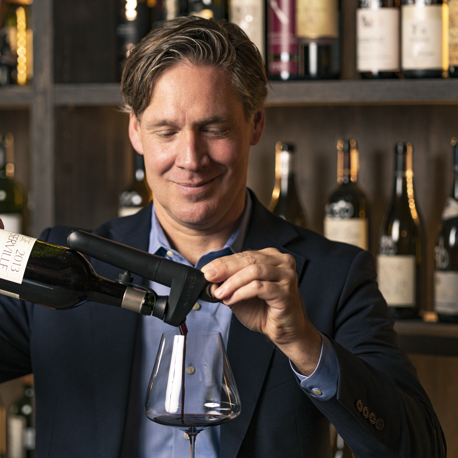 Man pouring wine with Coravin wine preservation system in front of wine bottles at a bar.