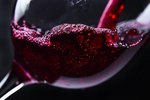 Close-up of red wine swirling in a glass, showcasing bubbles and rich ruby color against a dark background.