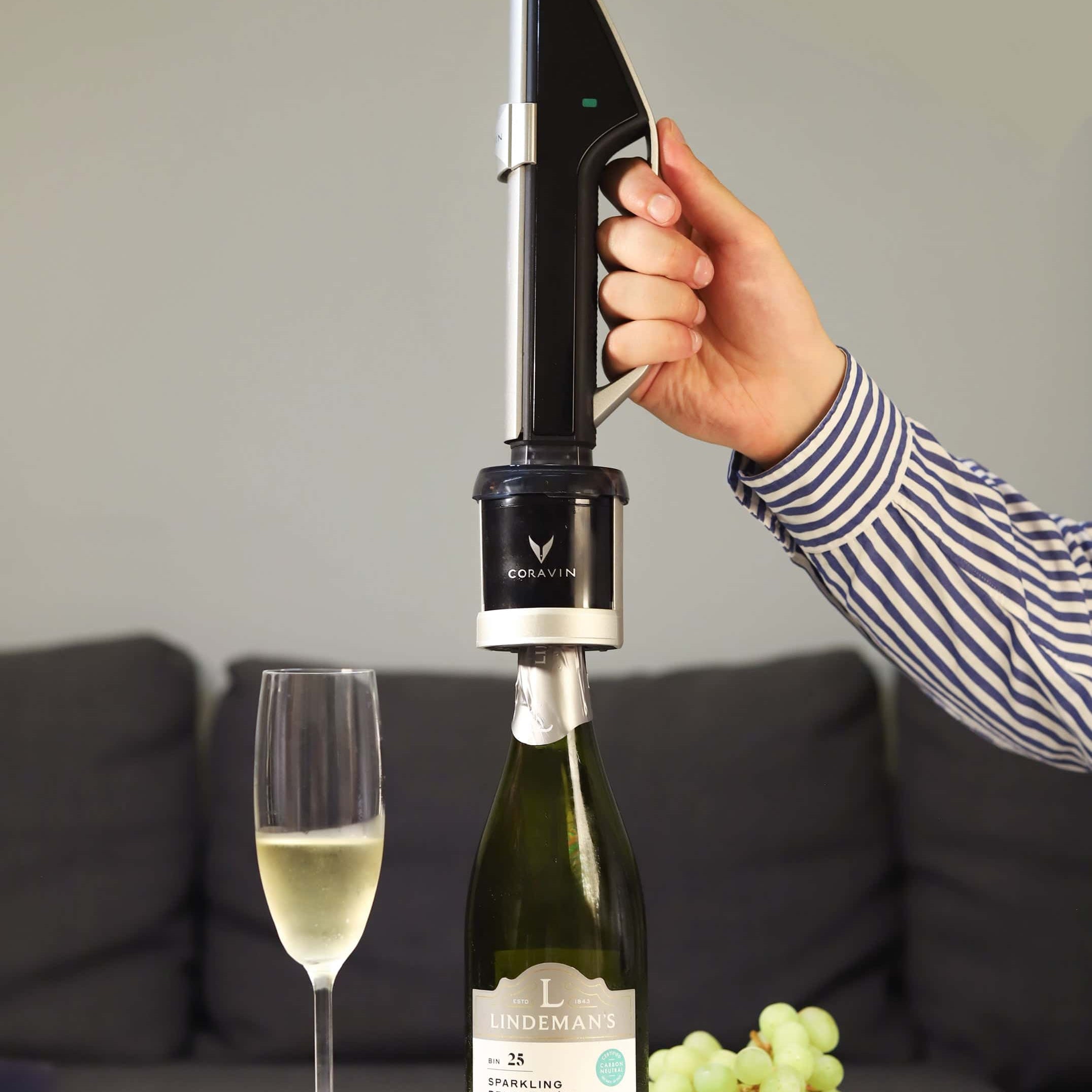Person using Coravin Sparkling System to pour Lindeman’s Brut Cuvée into a flute glass, with strawberries and green grapes on a table.