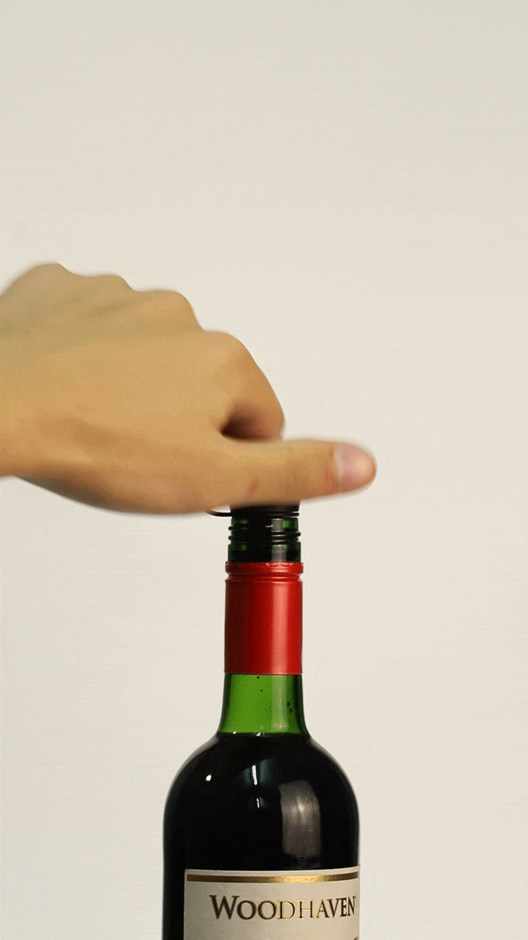 Hand removing the cap from a wine bottle labeled "WOODHAVEN," ready to pour.