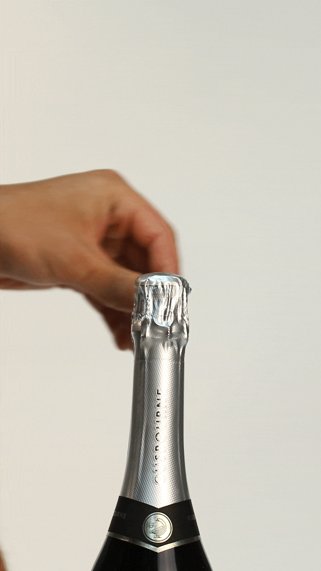 A hand removes the foil from a sparkling wine bottle, revealing a silver neck and label details.