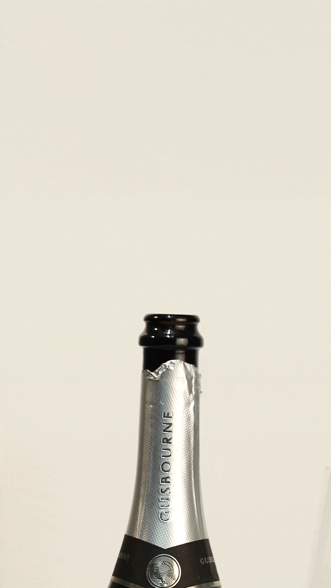 Close-up of a champagne bottle neck, featuring a silver label with "Gusbourne" printed on it.