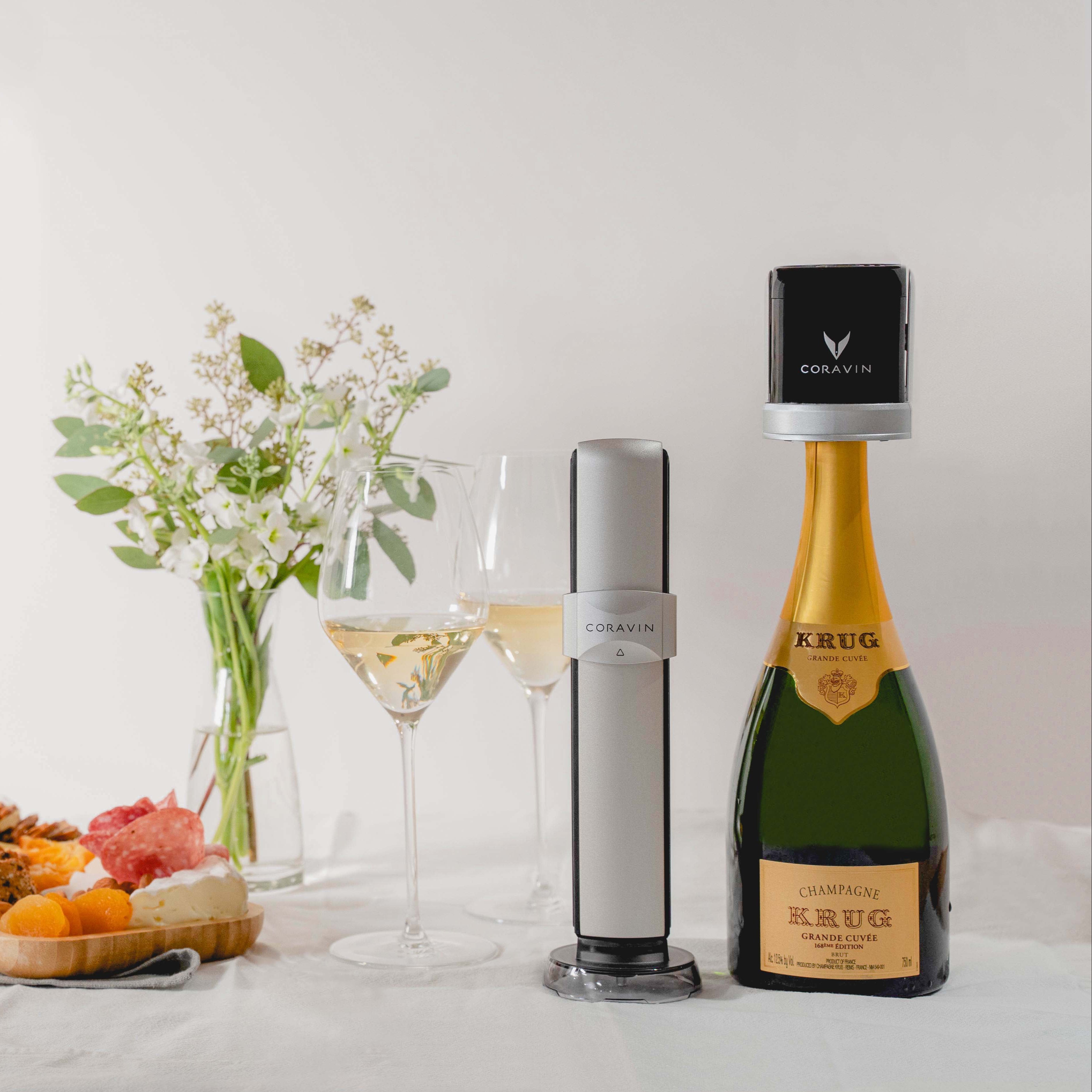 Coravin wine preservation system next to a bottle of Krug Champagne, two champagne glasses, and a flower arrangement.