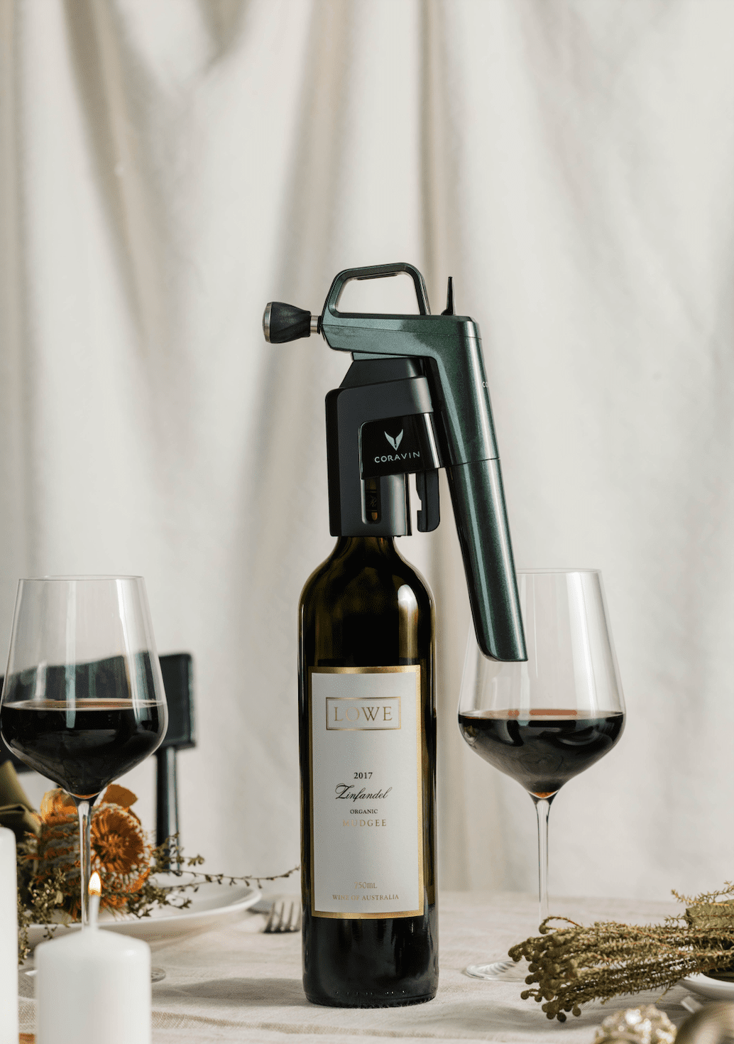 Coravin wine aerator on a bottle of 2017 Lowe Zinfandel, with two glasses of red wine and a candle in a dining setting.